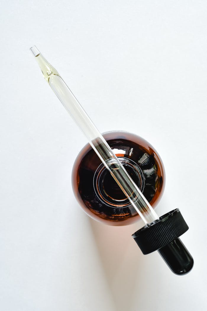A glass pipette and amber bottle on a white surface, perfect for skincare and essential oil themes.